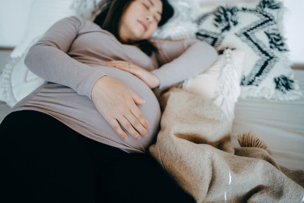 Asian pregnant woman holding her belly, sleeping on bed.