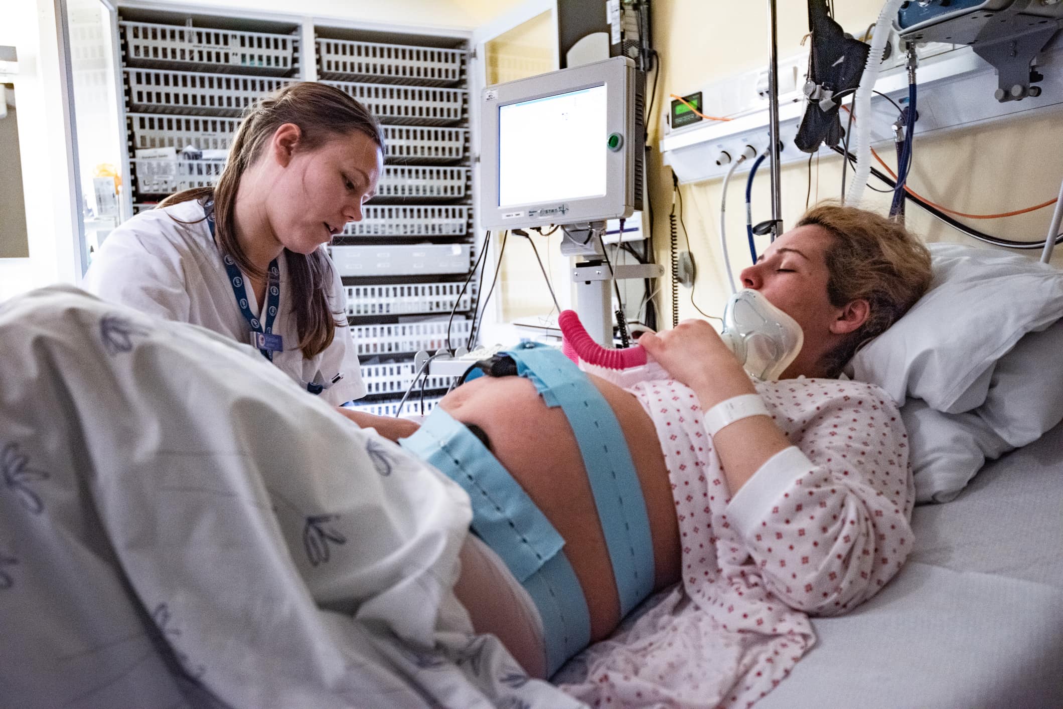 Pregnant woman lying down in a hospital bed and talking to a doctor.