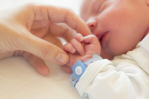 Newborn baby boy sleeping in his crib, his mother's hand holding his little hand.