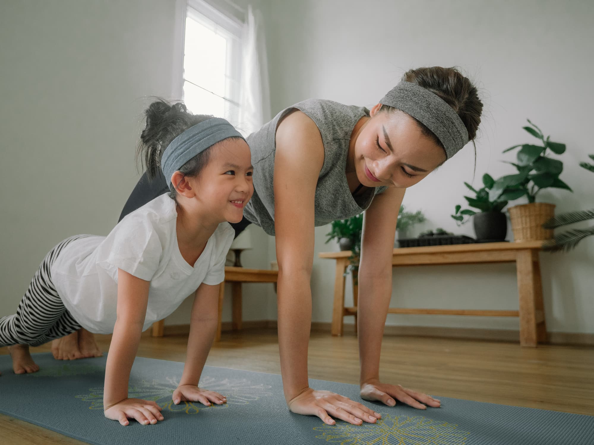 Young asian woman working out doing yoga with little girl at home