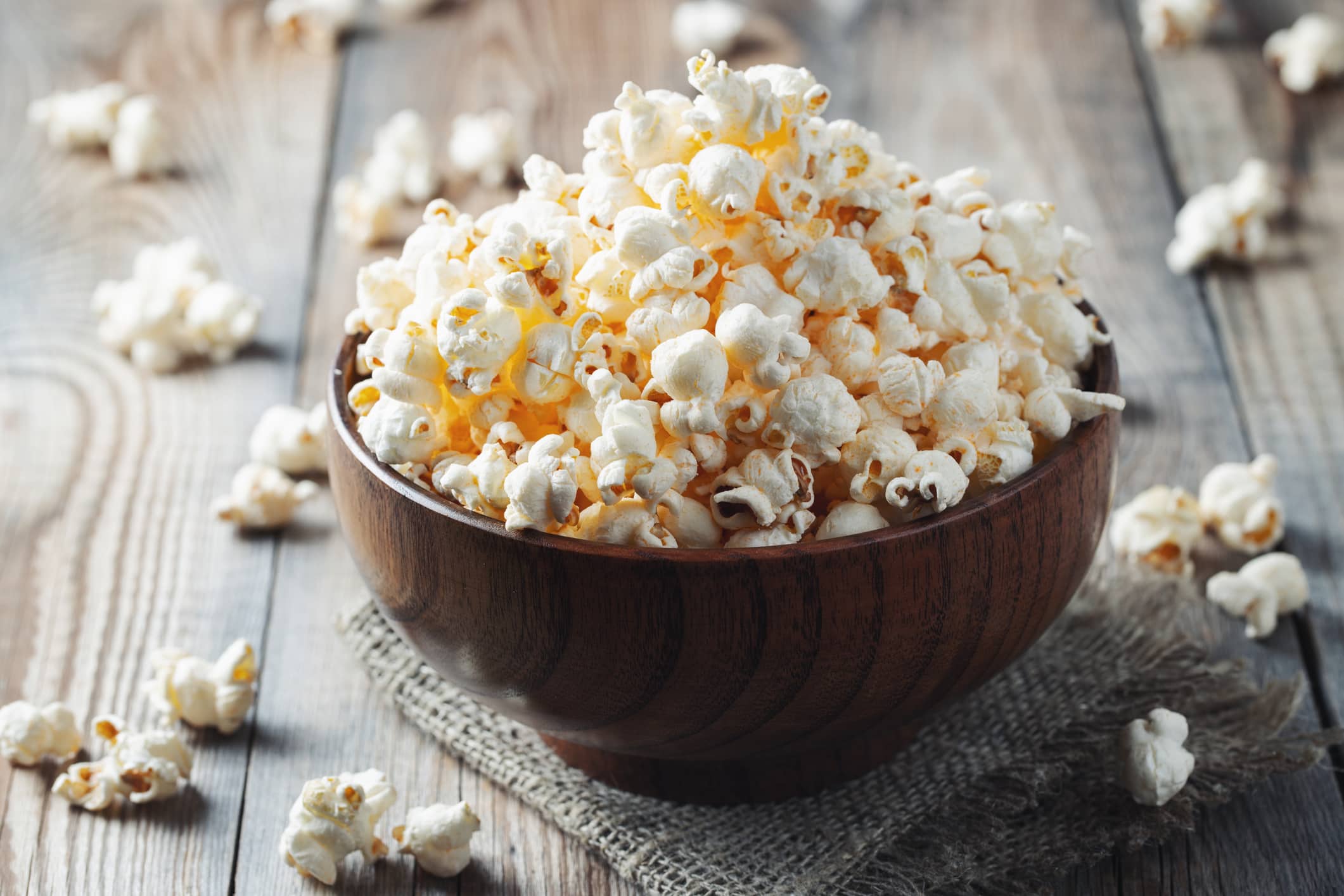 A wooden bowl of salted popcorn at the old wooden table. Dark background.