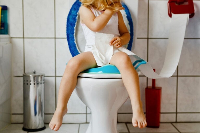 Closeup of cute little toddler baby girl child sitting on toilet seat.