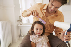 Father blow-drying his daughter's hair and brushing it.