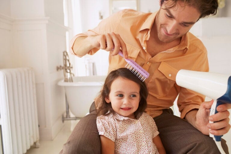 Father blow-drying his daughter's hair and brushing it.
