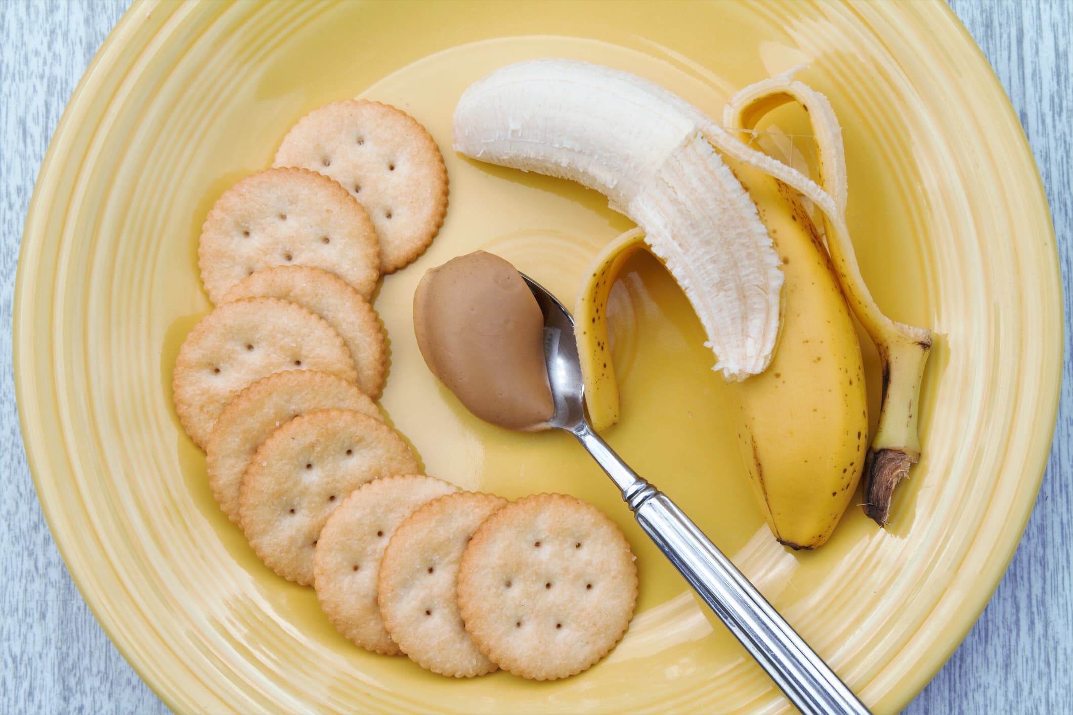 Peanut butter on spoon with banana and crackers.