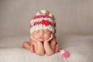 A newborn sleeping peacefully in a Valentine's Day themed hat.
