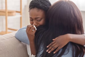 Condolence and support concept. Caring woman hugging her crying black girlfriend, comforting her after receiving bad news