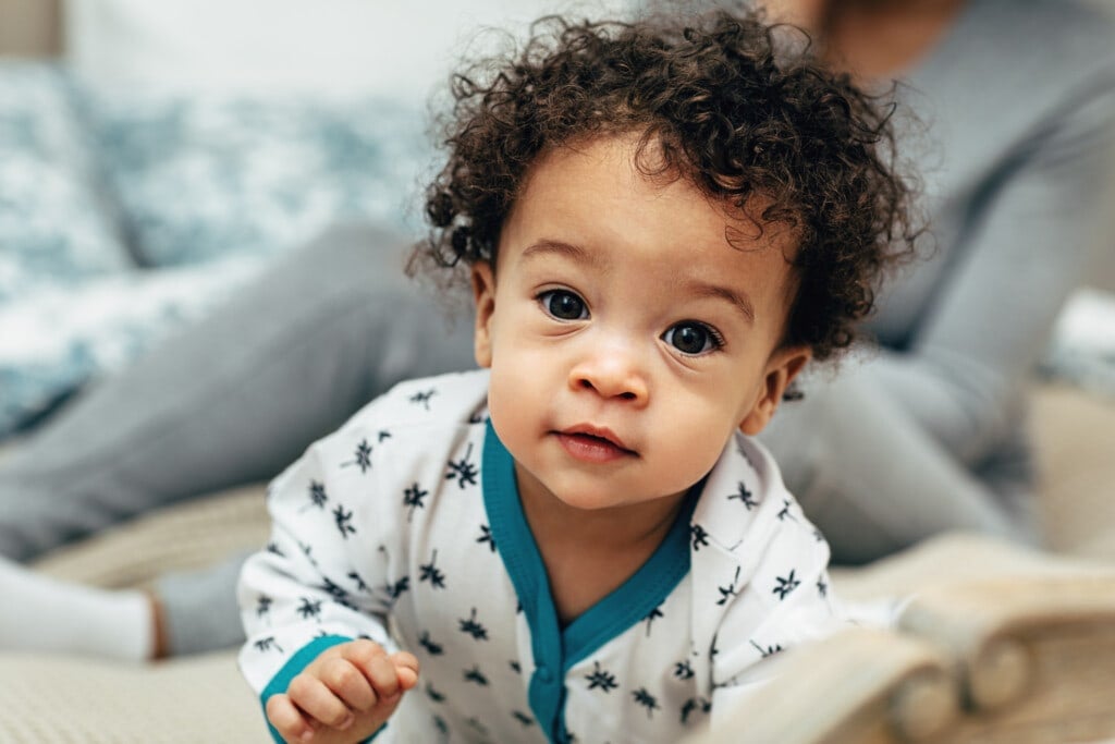 Close up portrait of a curly-haired baby boy crawling on bed.