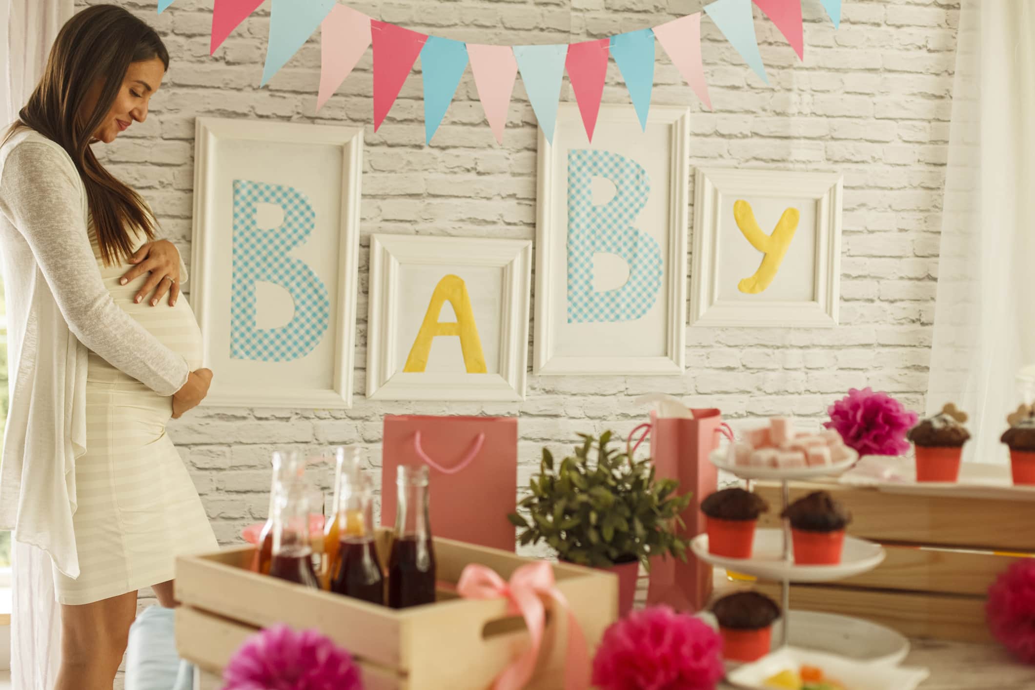 Selective focus shot of happy mom to be standing in front of a set up for her baby shower and holding her pregnant belly, contemplating and daydreaming about meeting her baby.