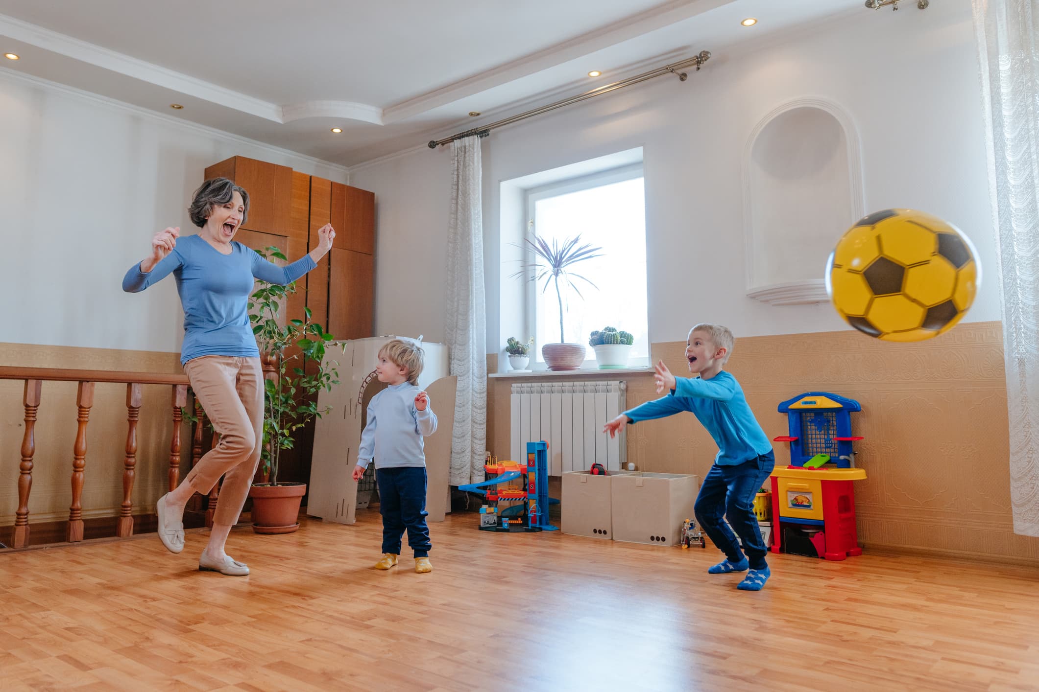 Active grandmother playing the ball with her grandchildren in the kids room indoor.