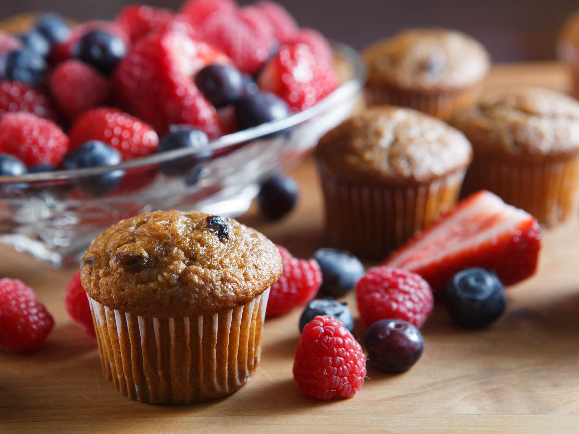 Blueberry Muffins with fresh raspberries, strawberries, blueberries on a wooden cutting board.
