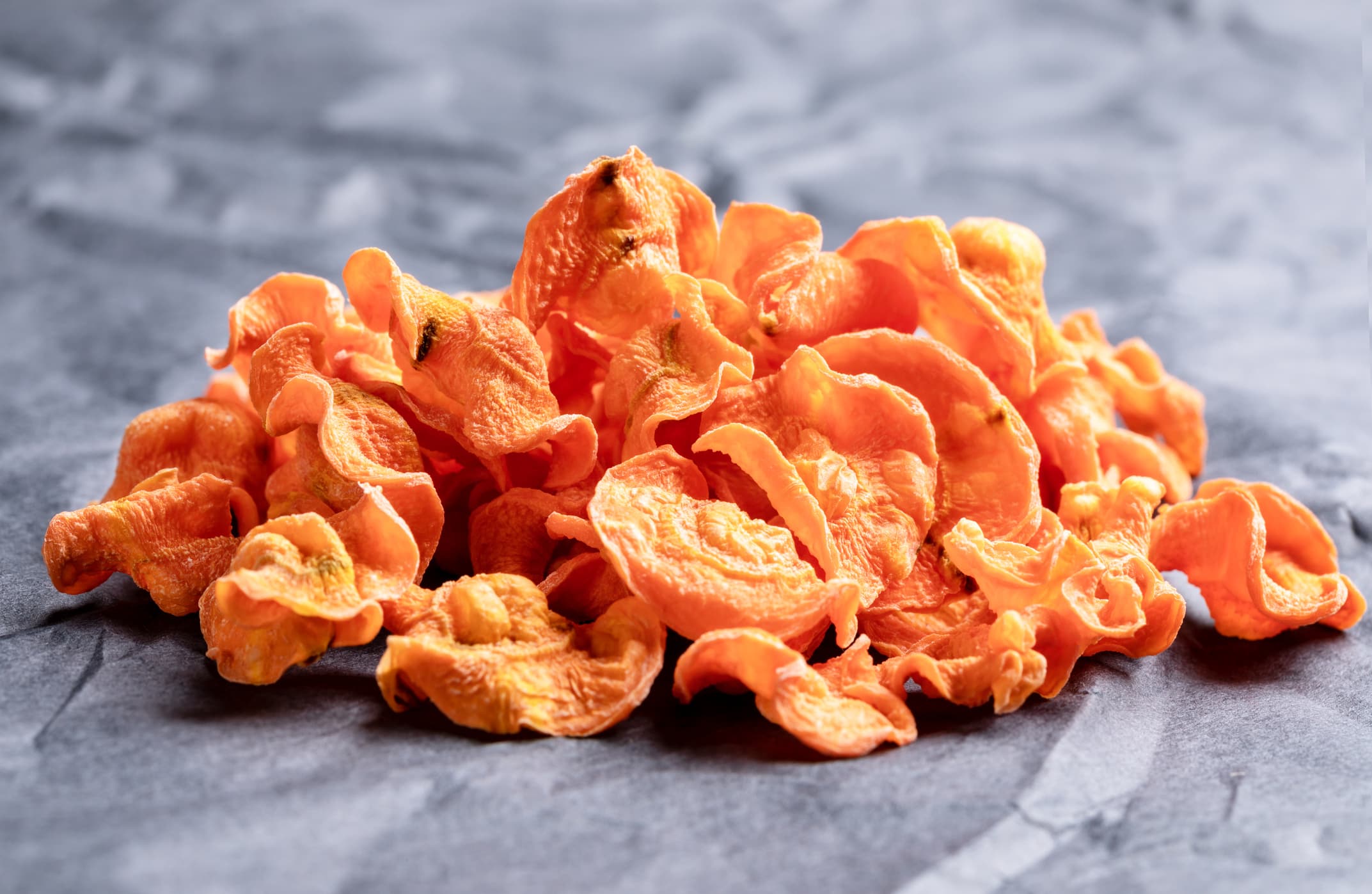 Front view to small bunch of orange vegetable carrot chips on rumpled black wrapping paper. Natural healthy vegetable snack. Alternative to ready-made chips.