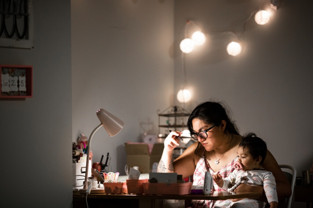 Authentic image of a mother working from home at her desk while holding her baby daughter. Shot in the late hours of the evening, the lighting creates the late night mood.