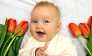 newborn baby girl boy laughing and showing thumb up among red tulips