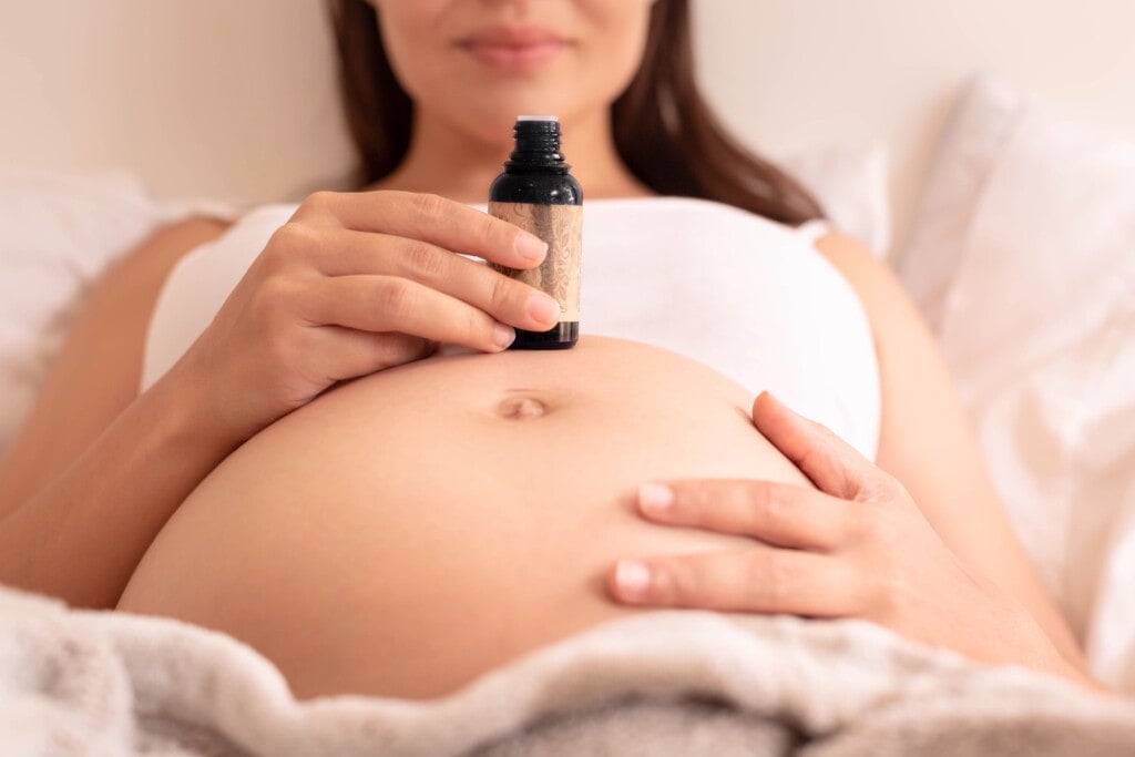 A pregnant woman using oil on her tummy and smelling essential oil for morning sickness and maternity health.