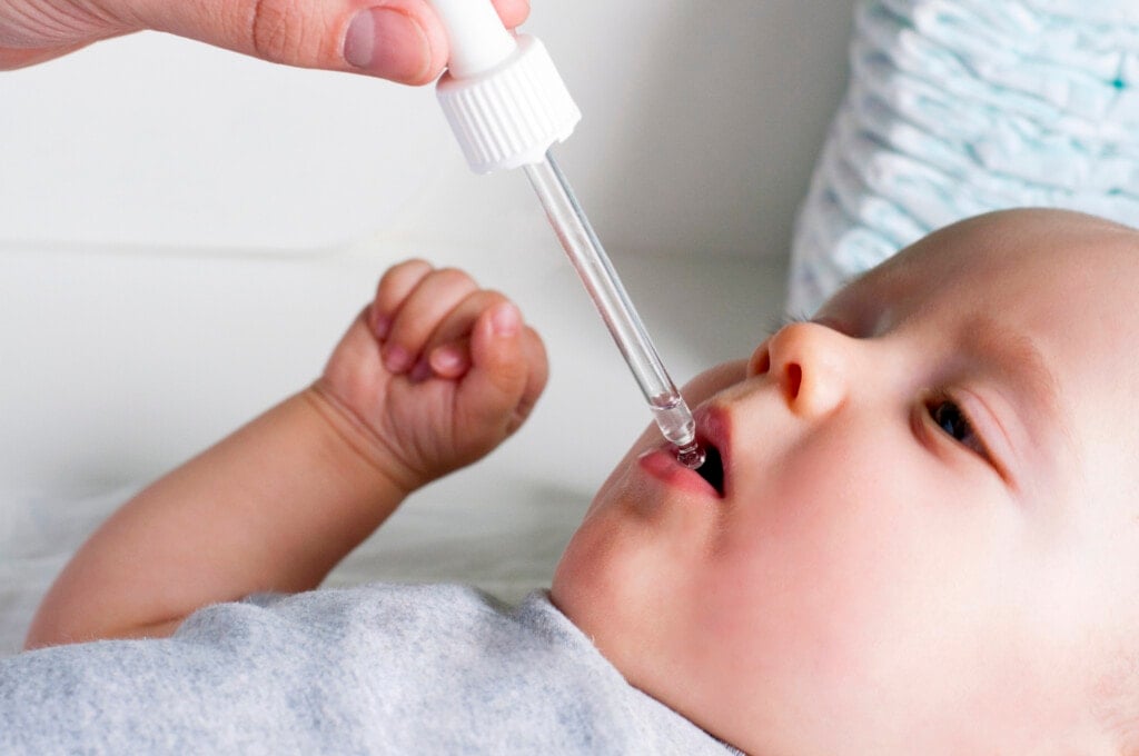 A young dad gives an infant baby liquid vitamins or medicine from a pipette.