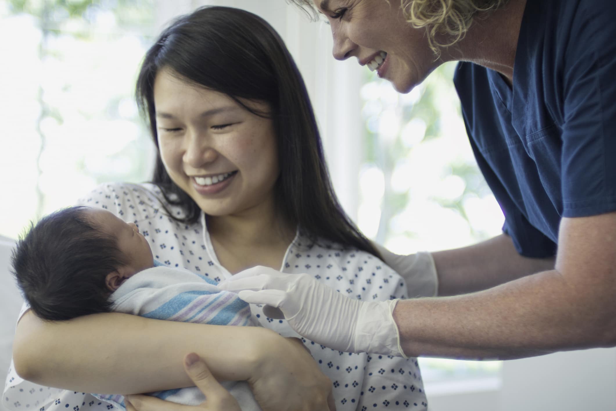 A woman of asian descent has just given birth in a hospital. In this frame a nurse is now handing her newborn child into her arms for the first time. Mom looks so proud and overjoyed to see her offspring after nine long months of waiting.