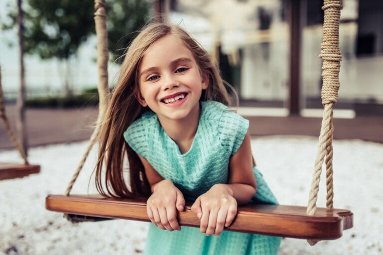 Charming little girl in beautiful dress is having fun on a swing. Smiling and looking at the camera.