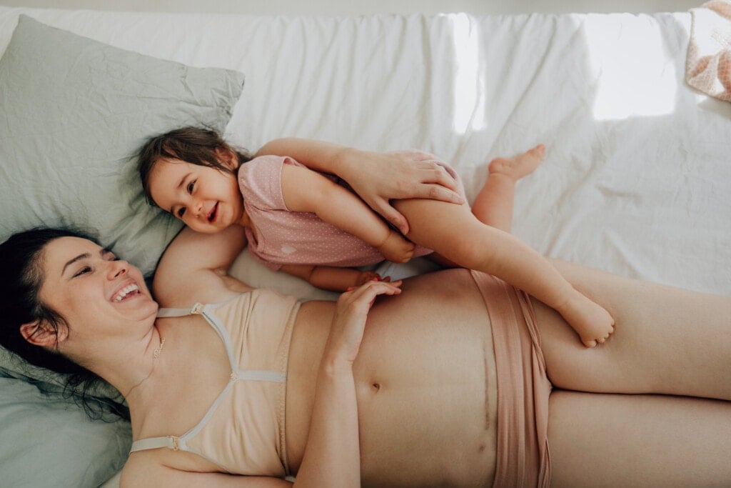 Photo of mother with c-section scar on a belly and her baby lying on the bed