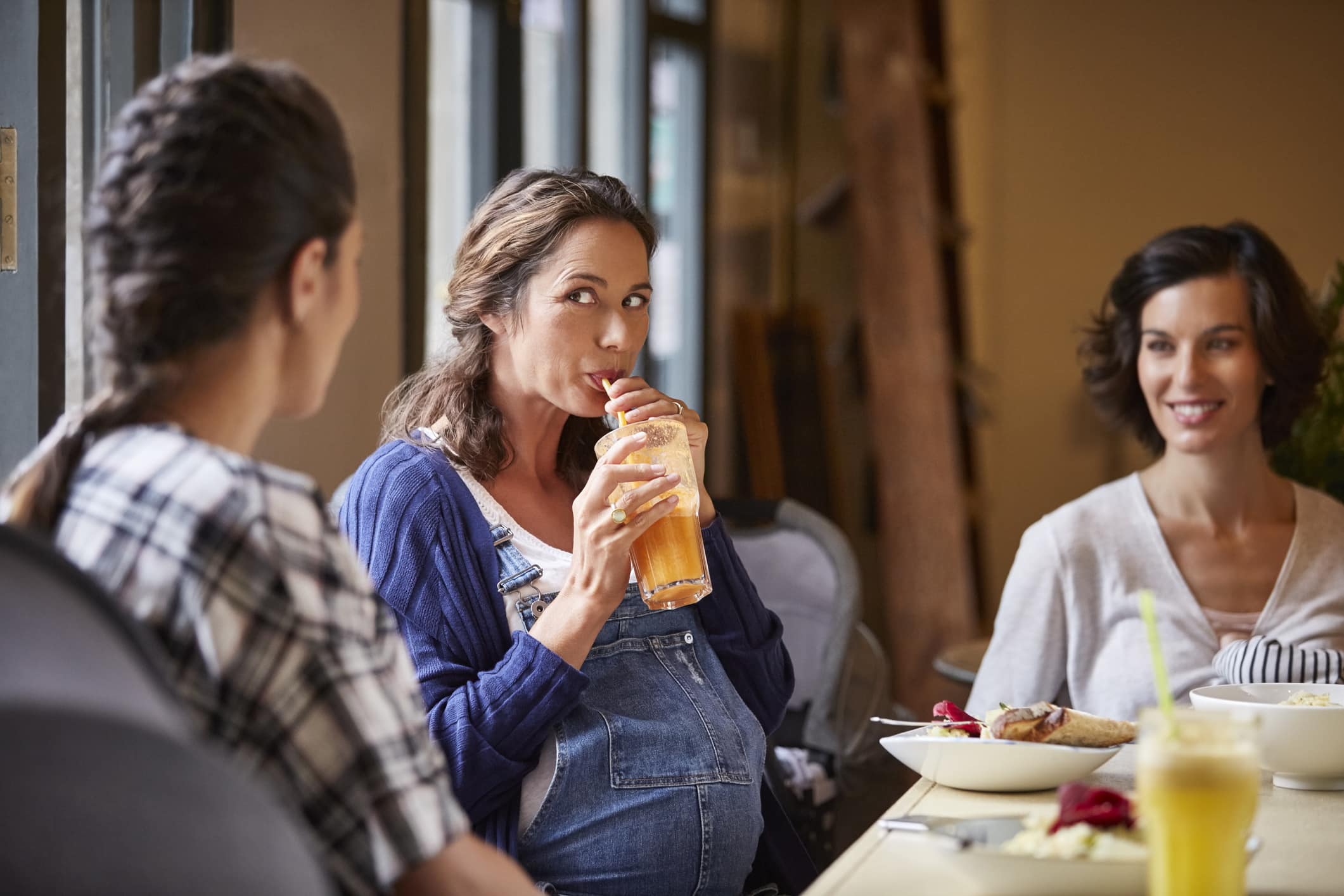 Pregnant woman drinking juice while sitting with friends at restaurant