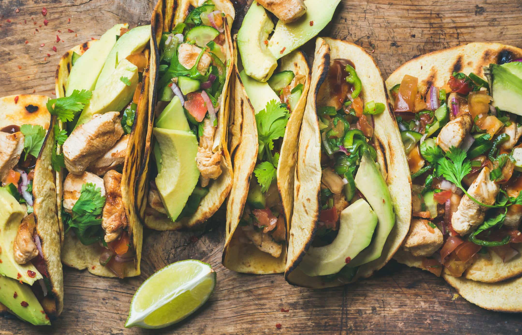 Tacos with grilled chicken, avocado, fresh salsa sauce and limes over rustic wooden background, top view. Healthy low carb and low fat lunch or food for company.