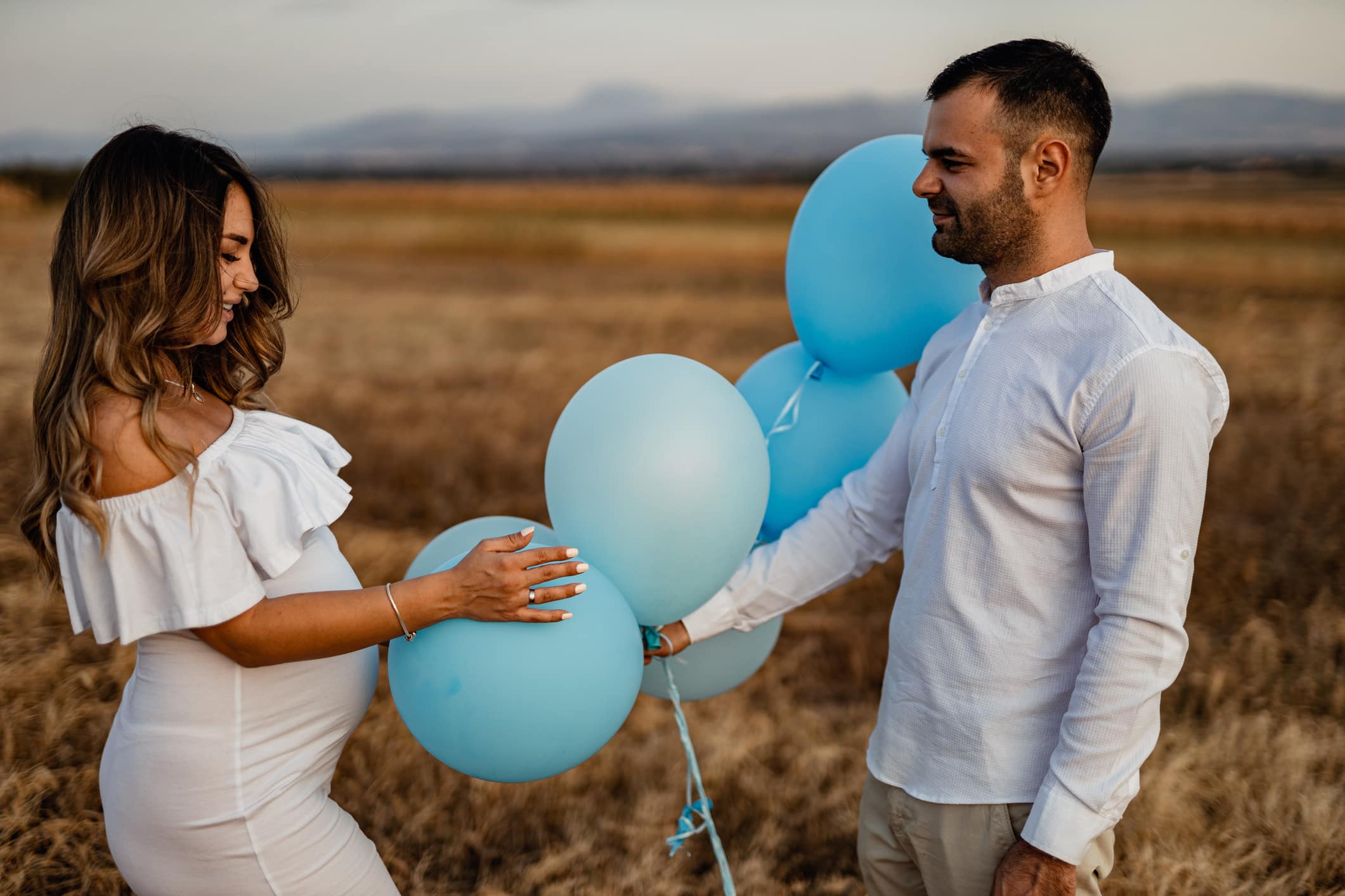 Beautiful young couple, pregnant wife and husband holding blue balloons to revile baby gender in nature on a sunny summer day