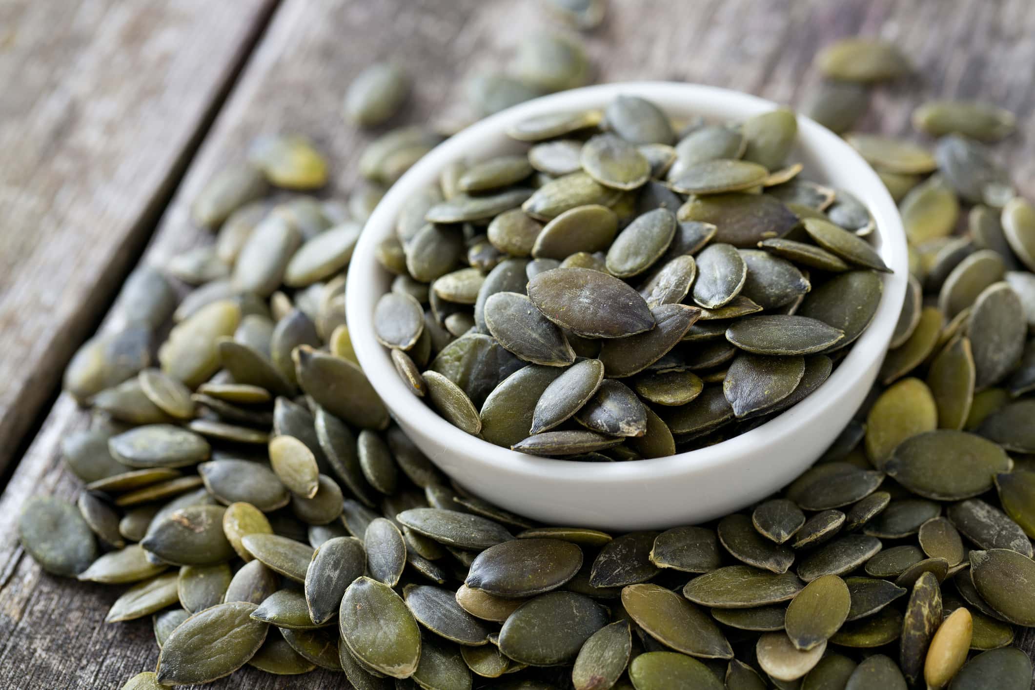 pumpkin seeds in a bowl on wooden surface