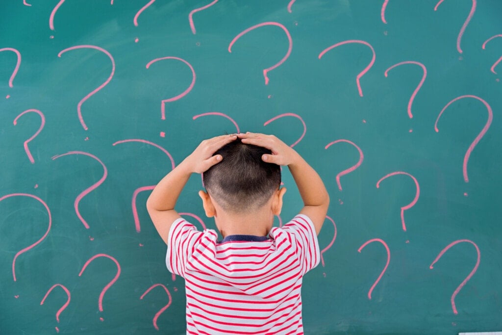 Asian little boy in front of blackboard with question marks.