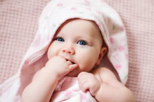 Authentic portrait of 4 months baby girl wrapped in hooded towel after bath. Horizontal image in soft pink tones.
