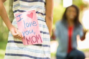 Happy Mother's Day. Little girl gives homemade card to her mom in front yard of family home.