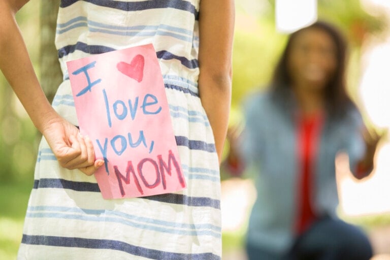 Happy Mother's Day. Little girl gives homemade card to her mom in front yard of family home.