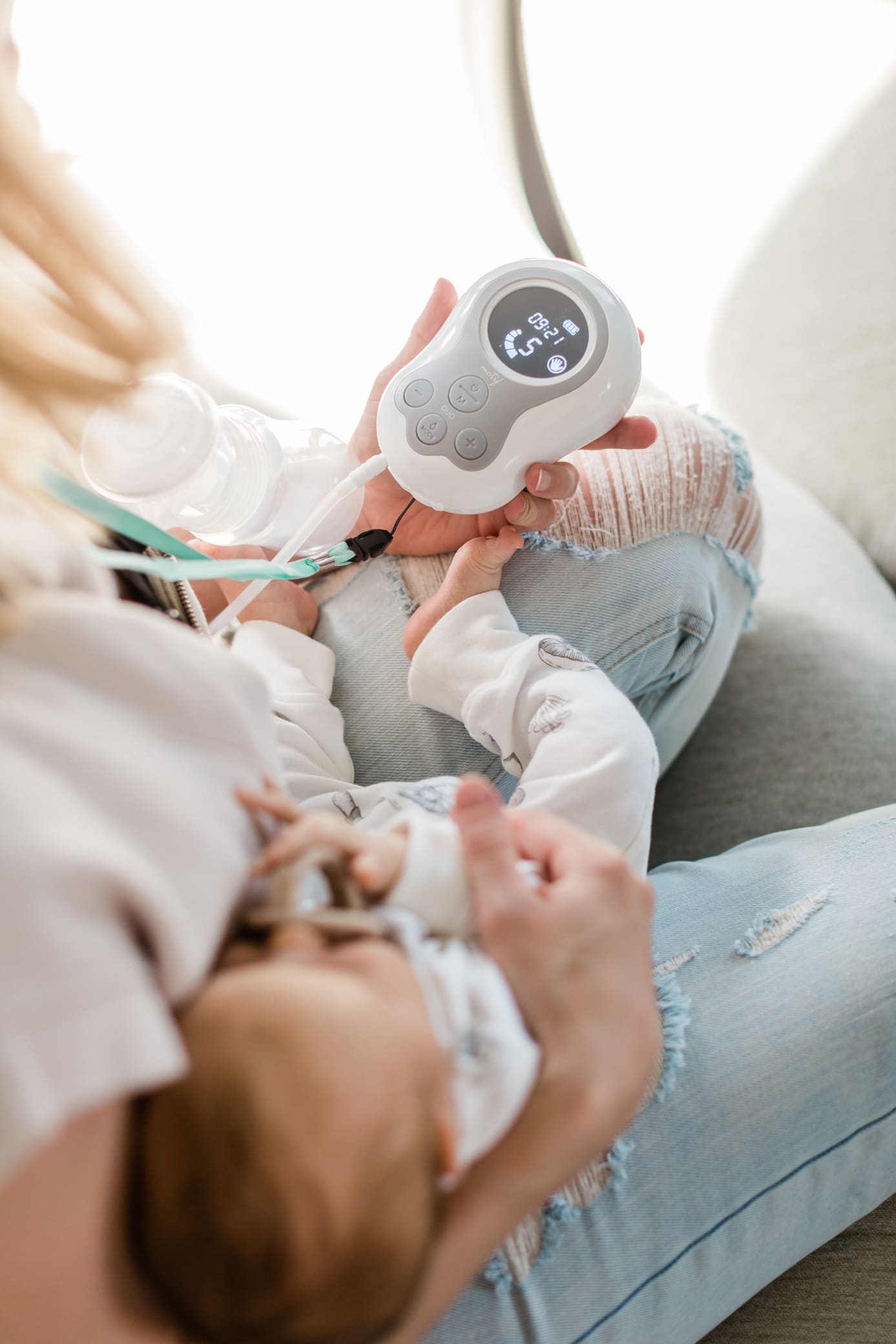 Mom sitting down holding her baby and pumping on her other breast with the Motif Duo pump.