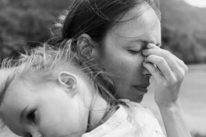 A sad mother covering her face depressed and unhappy holding her child in black and white.
