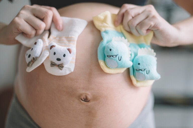 closeup on asian chinese pregnant lady holding 2 pairs of baby booties in front of her belly who expecting twin babies delivery