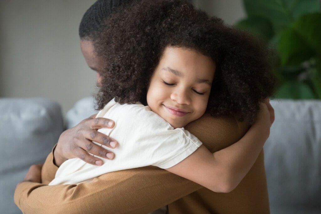 Cute funny mixed race child daughter embracing black father holding tight feeling love connection affection concept, happy african family dad and little kid girl hugging cuddling bonding at home