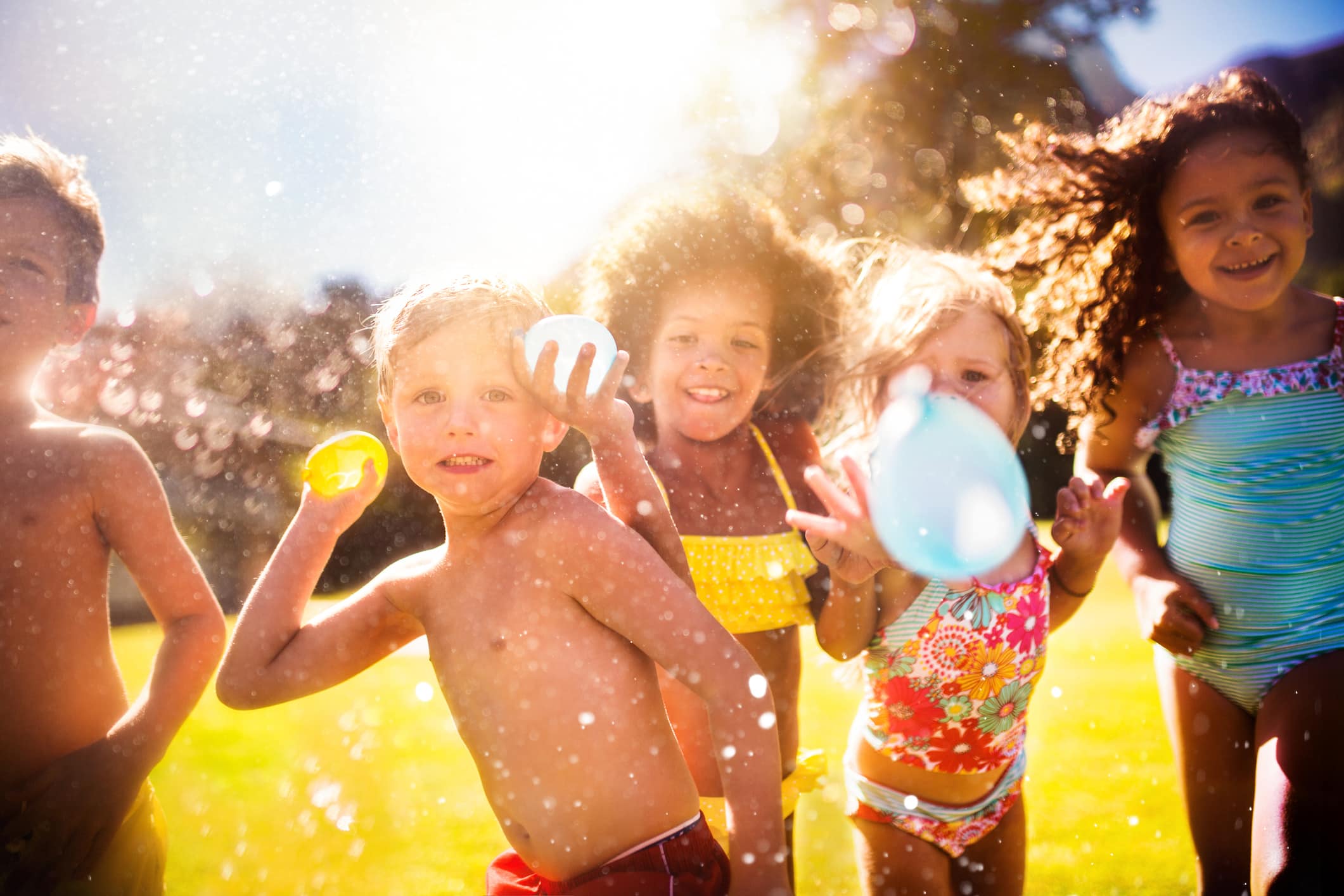 Happy mixed racial group of kids playfully throwing water balloons straight at the camera