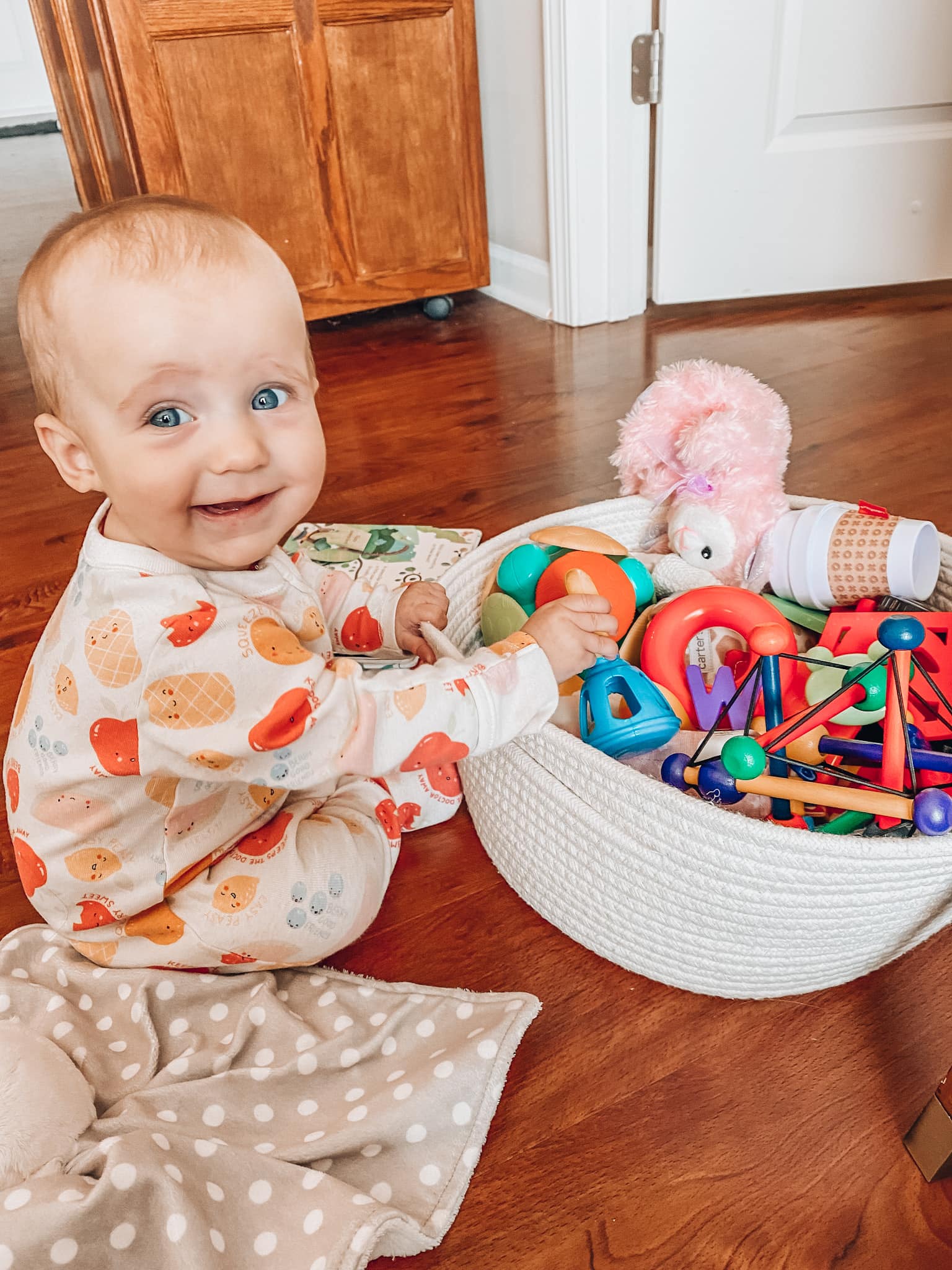 Baby girl sitting up holding a toy basket.