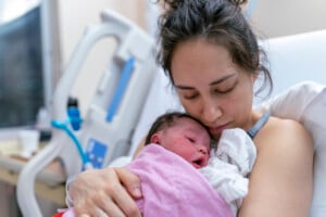 A beautiful and relaxed ethnic mother is snuggling her newborn and affectionately holding her in the hospital after delivery.