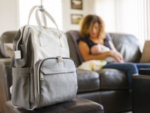 A young mother with her newborn baby girl inside a home. Image of diaper bag in front in focus.