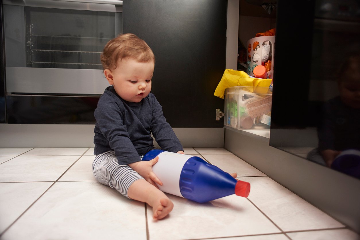 Baby boy opens up kitchen cupboard and pulls out the bleach from under the sink while his parents are distracted.