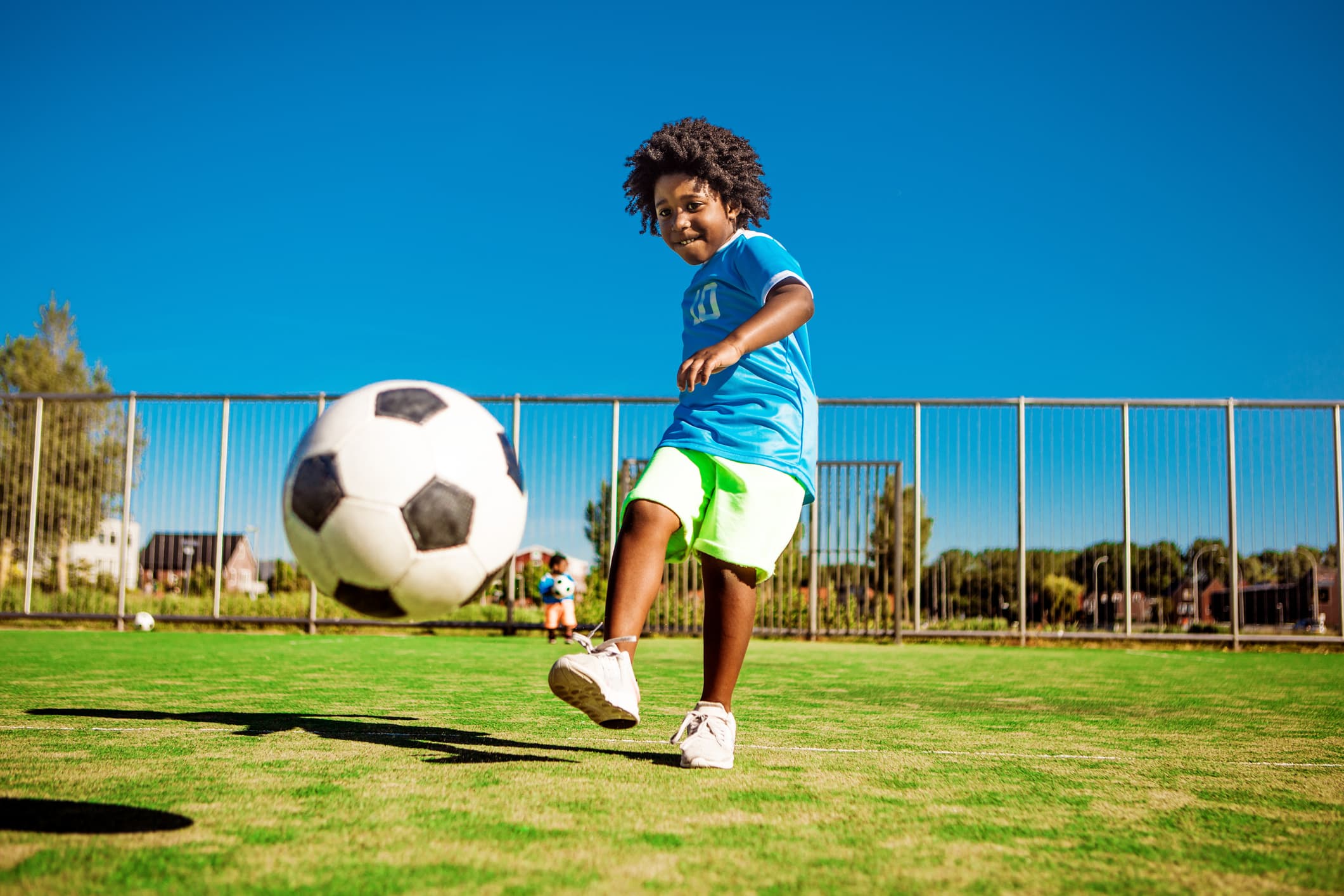 A young black boy child playing soccer on a neighbourhood football pitch on a beautiful sunny day in the Netherlands
