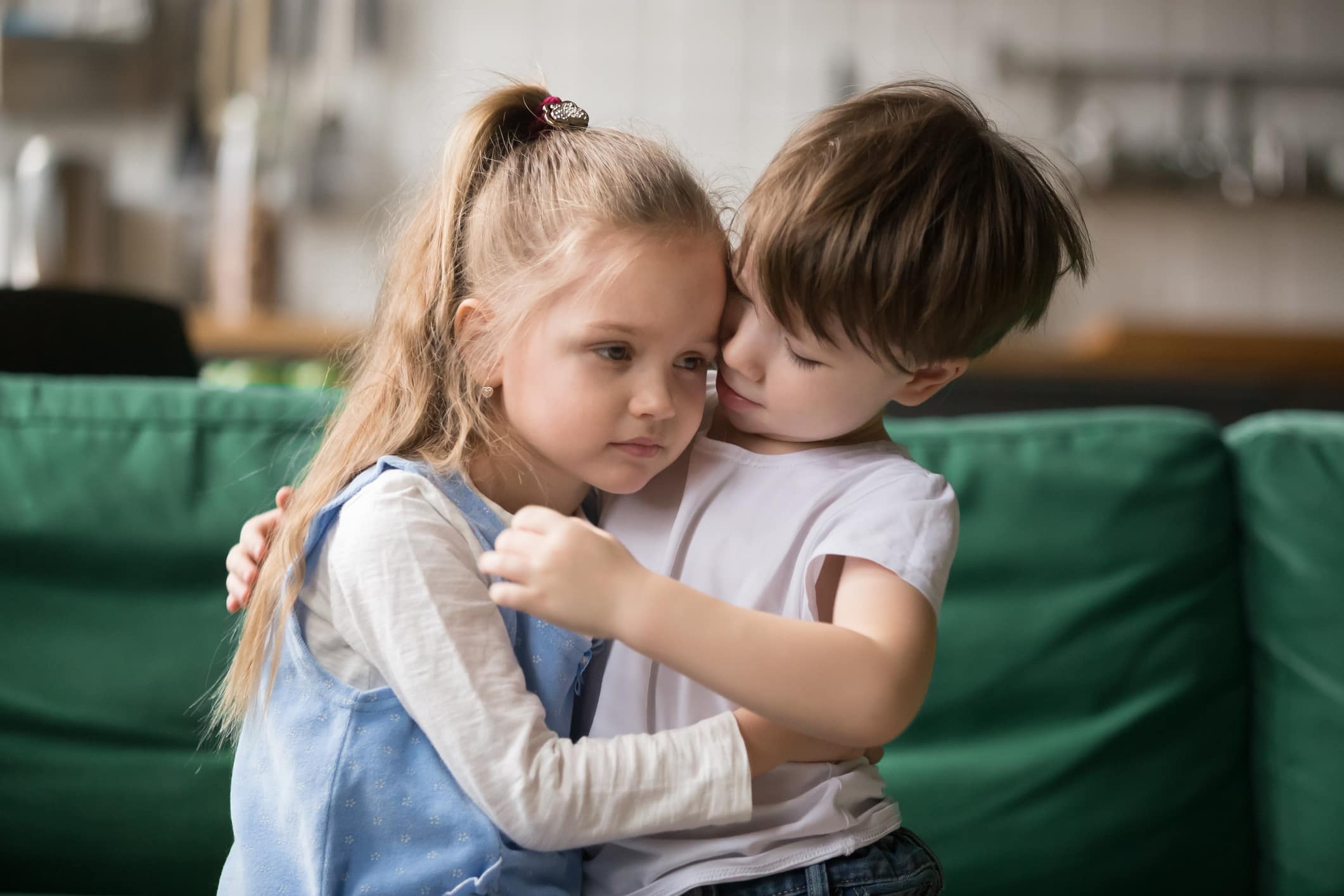Little boy hugging consoling upset girl sitting on sofa, kid brother embracing sad sister apologizing or comforting, siblings friendship, preschool children good relationships and support concept