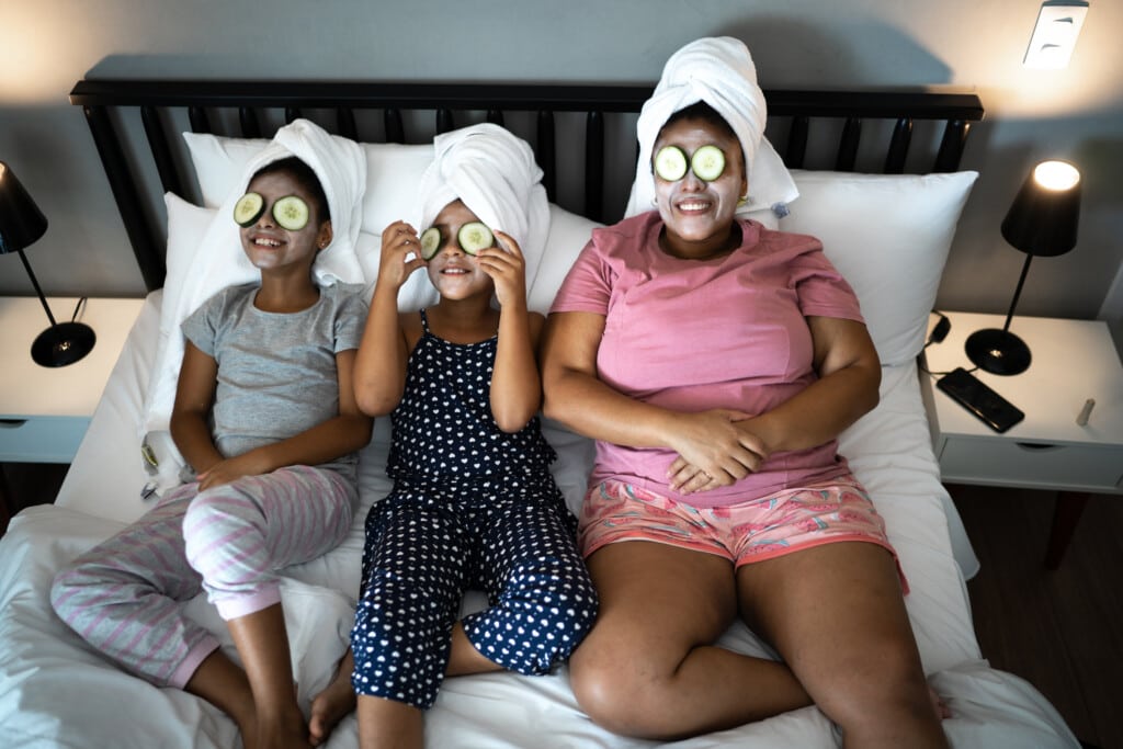 Mother and daughters in bed doing skin care with cucumber slices over the eyes