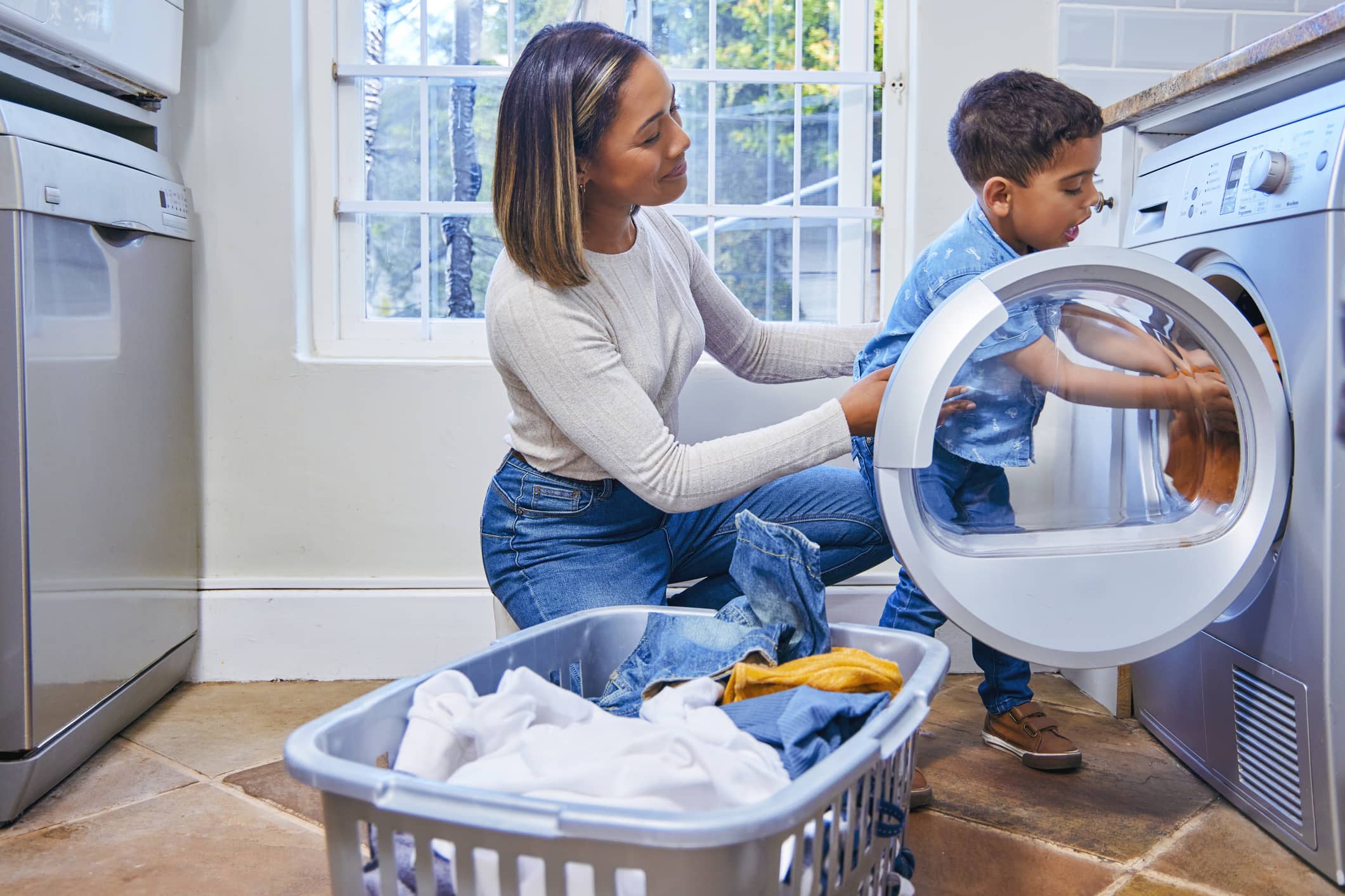 Young boy emptying the dryer and his mom kneeling behind him helping.