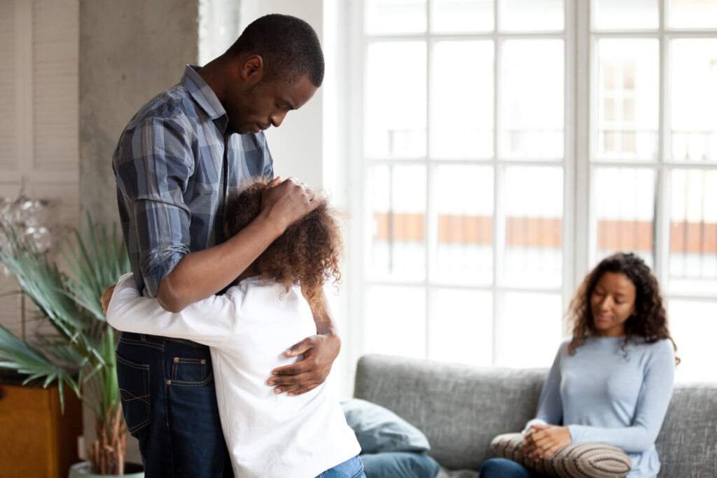 Unhappy African American family in living room at home, sad father embracing little preschooler daughter, child stay with mother, dad leave, saying goodbye, parents divorce, break up concept