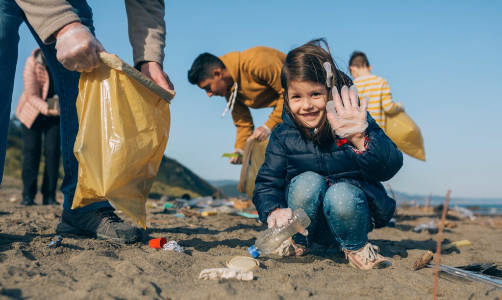 Little happy girl with volunteers picking up trash on the beach