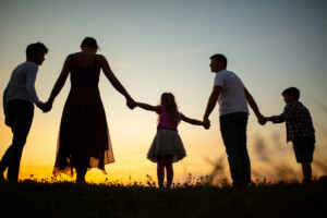 Family holding hands and walking together on grass field during sunset