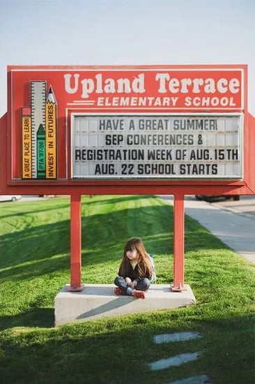 Little girl sitting outside in front of the school marquee.