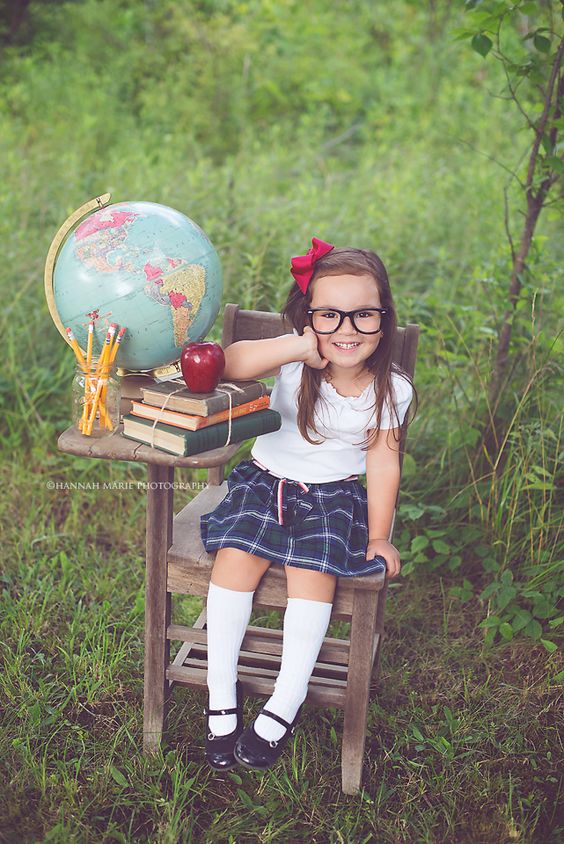 Little girl dressed up sitting at a school desk with some props outdoors for a back to school photoshoot