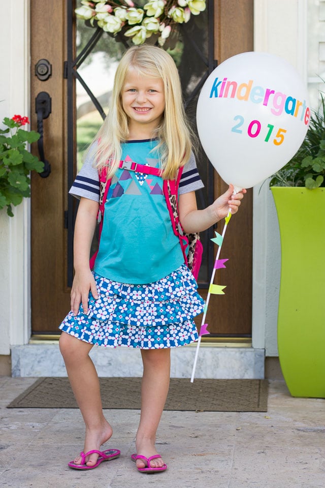 Girl standing at her front door holding a balloon up saying that she is going to Kindergarten.